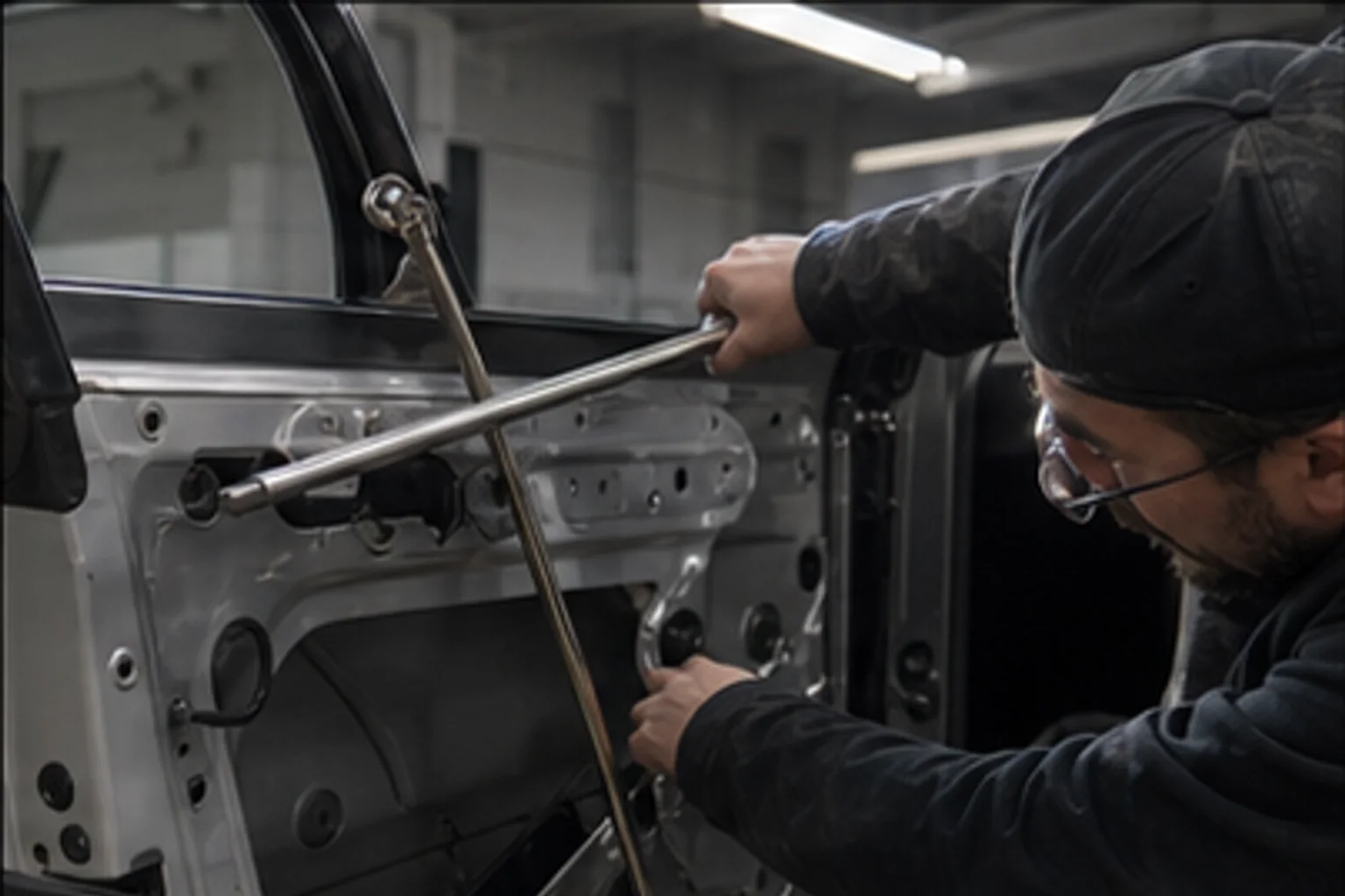Technician removing a dent with PDR rods under a striped reflection board